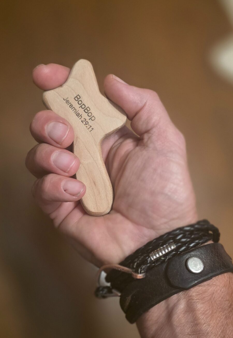 A person holding a handcrafted wooden prayer cross engraved with Jeremiah 29:11
